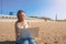 Beautiful smiling college woman having online video call on notebook while resting on the beach in sunny summer day.