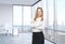 Beautiful smiling employee is standing in the office with New York panoramic view.