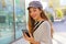 Beautiful smiling fashion woman with baker boy hat walking in the street and receive good news on her smart phone