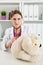 Beautiful smiling female doctor in white coat examine teddy bear