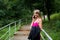A beautiful smiling girl in a pink dress with a jacke stands on the stairs in the forest and talks on the phone