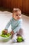 Beautiful smiling girl is sitting on a white plaid with plastic container with green apples