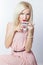 Beautiful smiling happy elegant girl with red lipstick in a pink dress in retro style drinks tea coffee from a small mugs