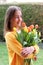 Beautiful smiling happy tween girl in yellow sweater holding and hugging big bouquet of bright orange tulips outdoors