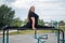 A beautiful smiling overweight young woman stretches for split on uneven bars outdoors. Fat girl gymnast doing fitness