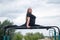 A beautiful smiling overweight young woman stretches for split on uneven bars outdoors. Fat girl gymnast doing fitness
