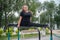 A beautiful smiling overweight young woman stretches for split on uneven bars outdoors. Fat girl gymnast doing fitness