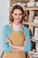 beautiful smiling potter with crossed arms standing near shelves with ceramic