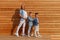 Beautiful smiling pregnant woman and two sons in grey pants and denim shirts on a wooden background