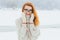 Beautiful smiling red head woman with glasses is wrapped in the scarf during the snowfall in the forest. Half-length