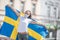 Beautiful smiling Swedish girl holds a flag while wearing a protective face mask outdoors