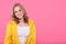 Beautiful smiling trendy teenage girl in bright yellow jacket looking at camera. Attractive young woman portrait over pastel pink.