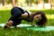 Beautiful smiling woman in morning park doing yoga and outdoor gymnastics. Green grass and rays of sun