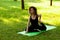Beautiful smiling woman in morning park doing yoga and outdoor gymnastics. Green grass and rays of sun