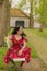 Beautiful smiling woman sitting on a bench in a red dress with blue flowers