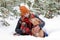 Beautiful smiling woman is sitting on a snow with her two dogs wrapped in red checkered plaid.