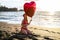 Beautiful smiling woman in summer hat and red swimsuit posing on the beach with heart balloon in hands