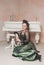 Beautiful smiling woman wearing green medieval vintage Victorian Style dress sitting on the floor near piano