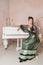 Beautiful smiling woman wearing green medieval vintage Victorian Style dress sitting near piano