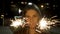 Beautiful smiling young woman holding a sparkler. Night scene. Young smiling girl holding sparkler in her hand. Holiday