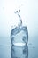 Beautiful splash, ice cube falling into the water, a glass with clean drinking water and a high splash with splashes of water