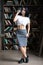 A beautiful sportive girl stands against the background of bookshelves. Pretty young librarian wearing glasses