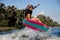 Beautiful sporty woman skillfully jumping over splashing river wave on surf style wakeboard.