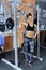 Beautiful sporty woman smiling and resting over barbell after a muscular training in fitness center