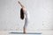 Beautiful sporty young woman doing standing backbend pose in white loft