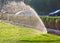 A beautiful spray fountain from an automatic sprinkler system sprays the green lawn on a bright sunny day