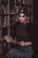 Beautiful stylish blonde woman in a knitted headband, jacket and culottes in a loft interior with a shelf with books. Soft