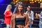 Beautiful stylish caucasian brunette woman in a bandanna looks at the camera while her friends dancing in colored disco