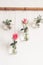 Beautiful stylish holiday decoration. Roses in vases jars are suspended from white wall.DIY romantic decoration, front