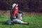 Beautiful stylish red haired fashion hipster model woman sitting outdoors on green grass at park wearing sunglasses, hat and black