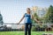 Beautiful stylish woman in a blue shirt and leggings stands near a football goal at the stadium at sunset. Beautiful sunlight. A g