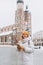 Beautiful stylish woman in hat walking on Market Square in Krakow in winter day and holding mobile phone. Urban