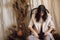 Beautiful stylish woman in suit sitting on retro wooden chair in bohemian style room with dry grass