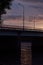 Beautiful summer evening with sunset sky, golden sunbeams, blue clouds, black silhouette bridge with lanterns lights over river.