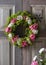 Beautiful summer flower wreath made of pink and white roses and lady`s mantle blossom hangs on old weathered wooden door.
