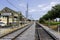 A beautiful summer landscape at the Dumaine Street RTA station with railroad tracks, parked cars, lush green trees and grass