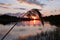 Beautiful summer sunset and pink sky over river. Clouds are reflected in calm water. Tall grass in foreground in the rays of