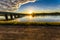 A beautiful sunrise over a wide river next to a long green bridge