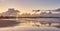 Beautiful sunset on the beach with water reflections, seagulls on the sand and windmills on background