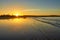 Beautiful sunset on the beach with water reflections, seagulls on the sand and windmills on background