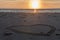 Beautiful sunset at the beach with wooden piles and hearts drawings in the sand
