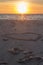 Beautiful sunset at the beach with wooden piles and hearts drawings in the sand