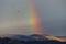 Beautiful and surreal view of part of a rainbow over some hills with birds flying