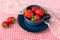 Beautiful, sweet, freshly picked strawberries in a ceramic cup on a red-and-white checkered tablecloth
