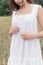 Beautiful sweet girl with dark hair in a white summer dress sundress walking in a field with spikelets with a white ribbon in her