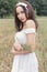 Beautiful sweet girl with dark hair in a white summer dress sundress walking in a field with spikelets with a white ribbon in her